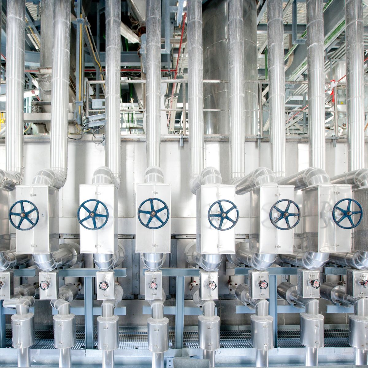 A symmetrical view of industrial pipes and valve wheels in a chemical manufacturing facility.