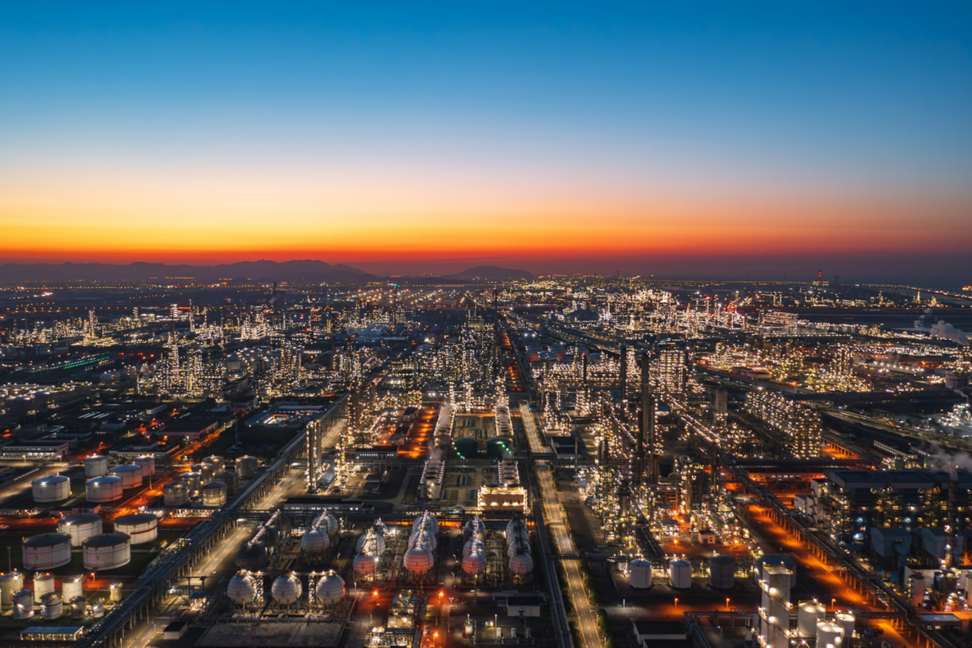 Panoramic view of a refinery facility illuminated at dusk, showcasing large-scale industrial operations, energy production, and infrastructure at night.