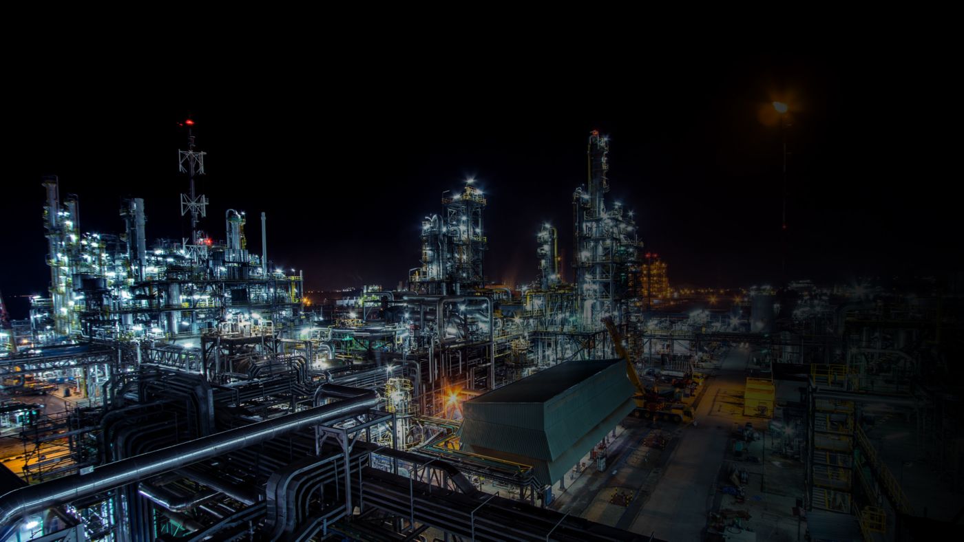 Nighttime view of an industrial refinery facility with illuminated processing units, piping networks, and operational infrastructure.