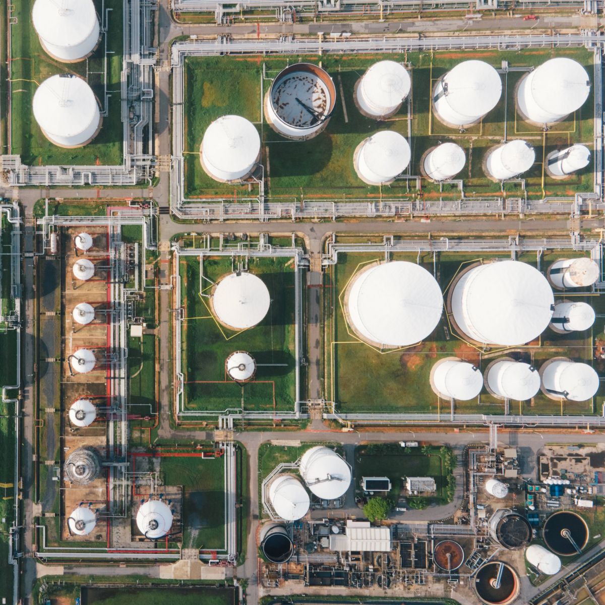An aerial view displays an industrial refinery with numerous storage tanks and a complex network of interconnected pipelines.