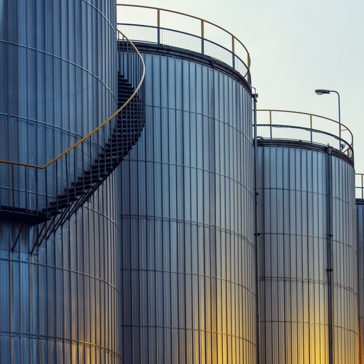 A series of corrugated metal industrial silos with helical staircases standing against a muted sky.