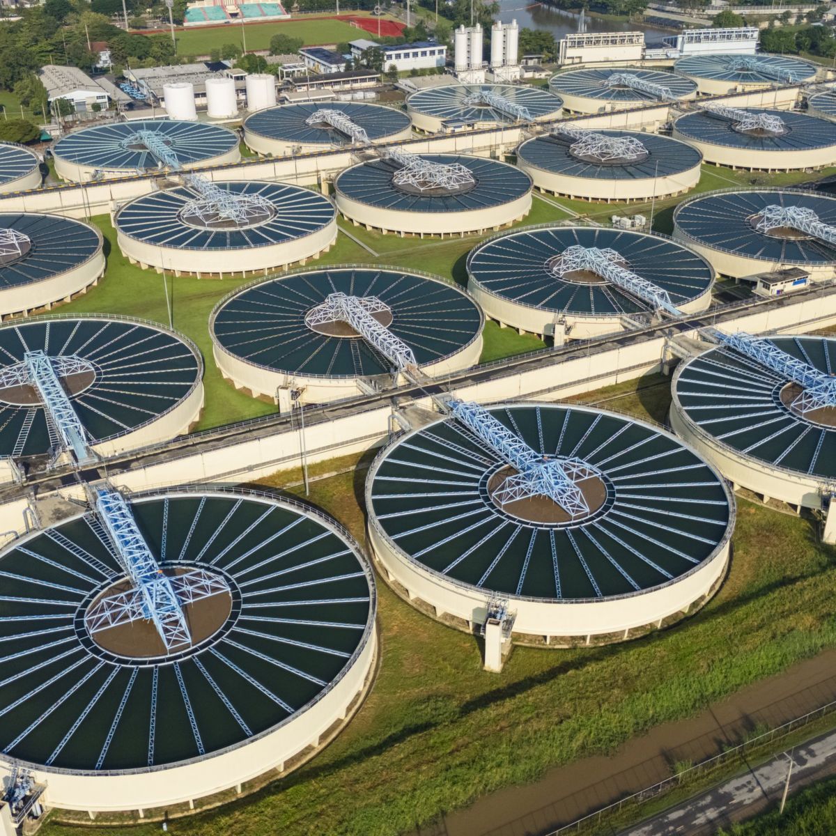An aerial view of a large-scale municipal wastewater treatment plant featuring numerous circular clarifier tanks arranged in a systematic industrial grid.