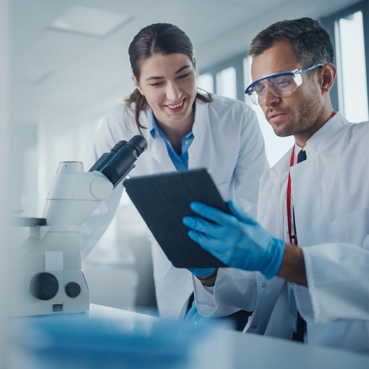 Modern Medical Research Laboratory: Portrait of Two Scientists Working, Using Digital Tablet, Analyzing Samples, Talking. Advanced Scientific Pharmaceutical Lab for Medicine, Biotechnology Development