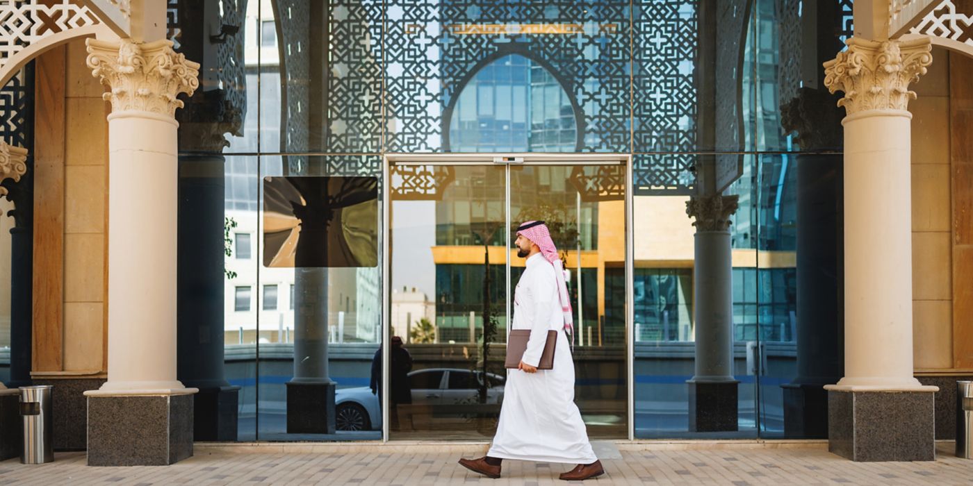 Individual walking along a modern building entrance with glass panels and decorative architectural facade design.
