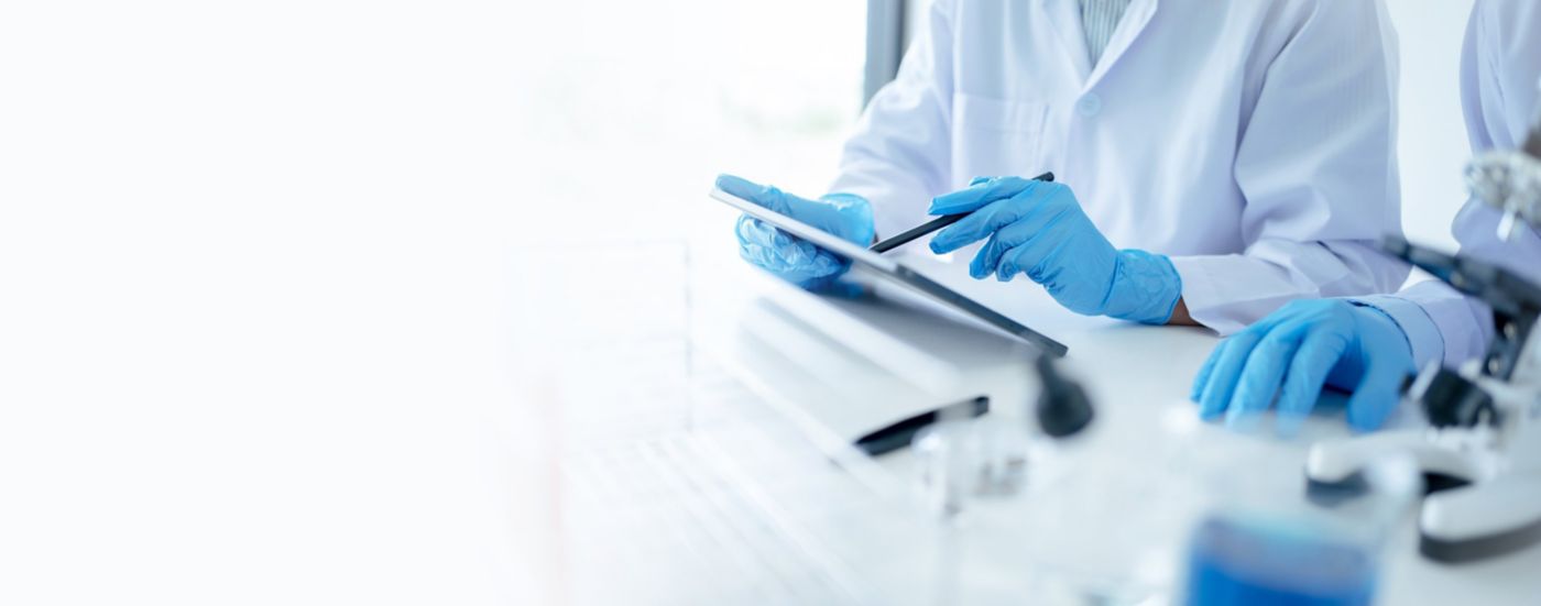 Blue-gloved hands use a tablet on a bright laboratory work surface.