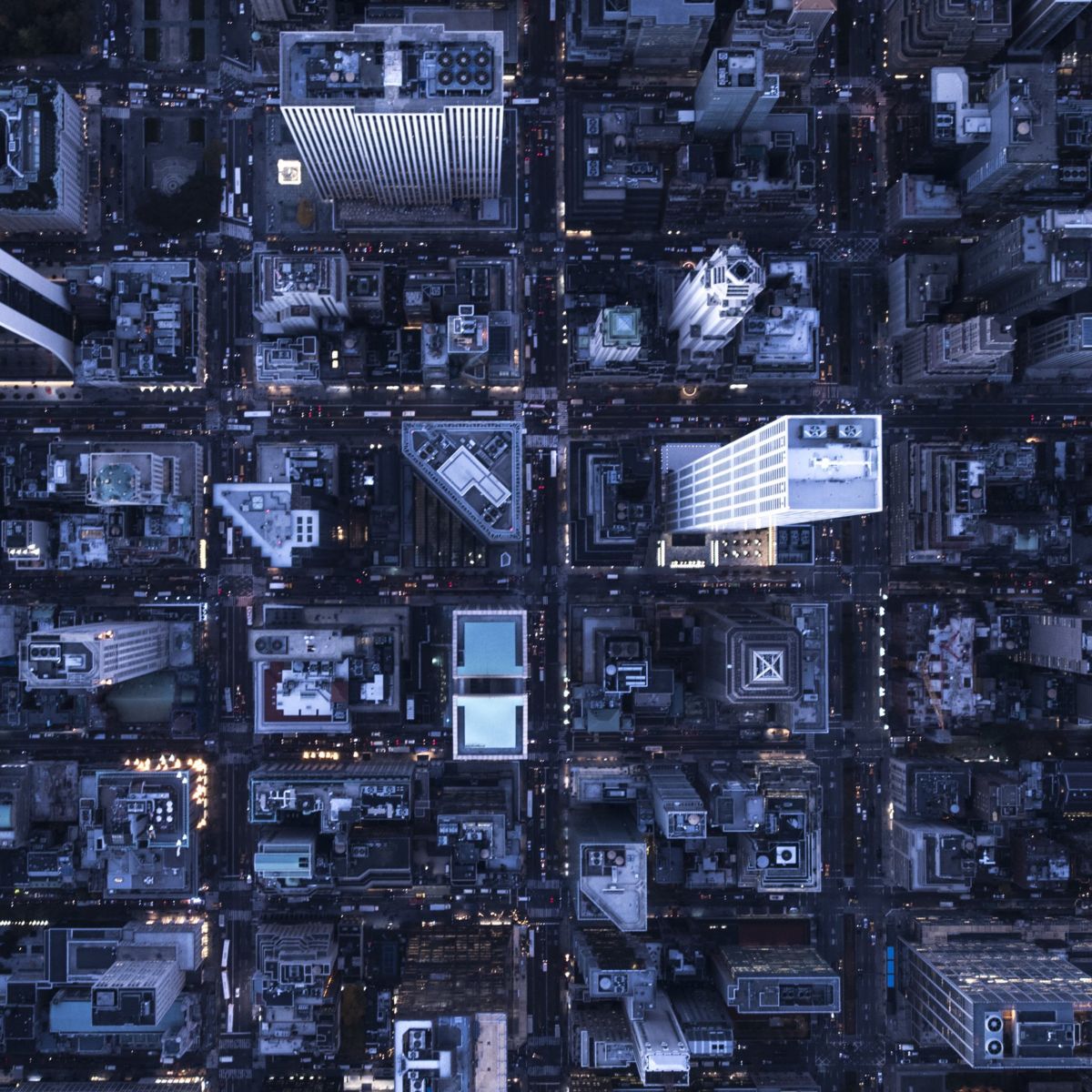 A high-angle aerial view of Manhattan city blocks at dusk, highlighting urban architecture and grid-patterned streets illuminated by evening city lights.
