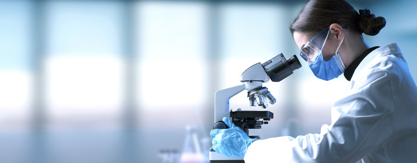 Researcher wearing a surgical mask and looking through a microscope, medical research and science concept
