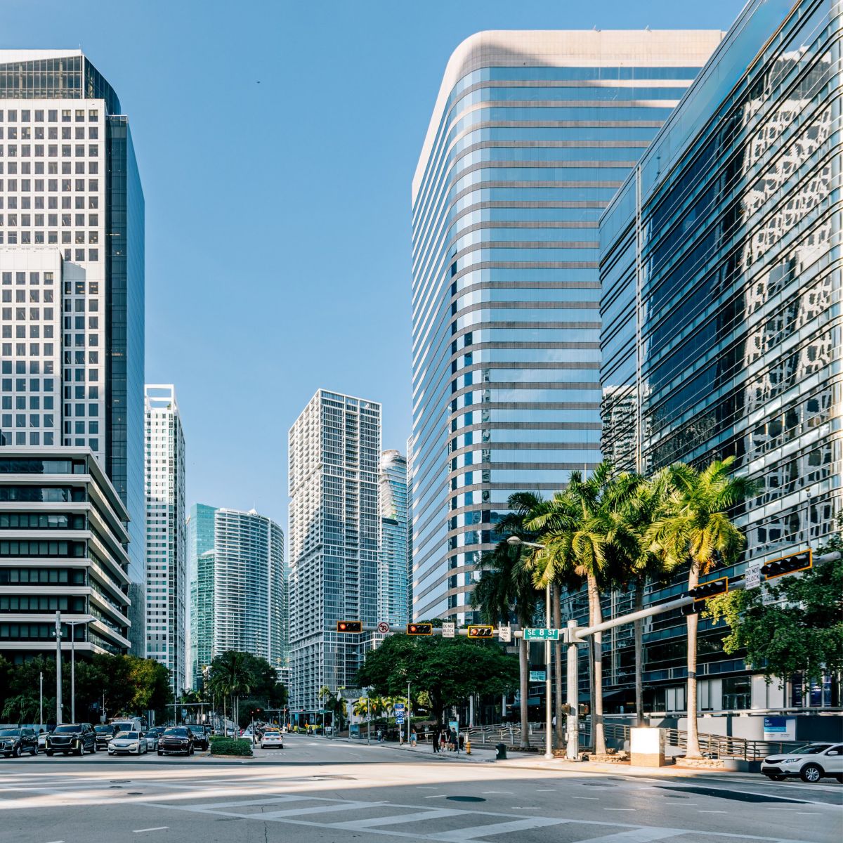 Modern corporate skyscrapers rise above a sunlit urban intersection in the vibrant business district of downtown Miami, Florida.