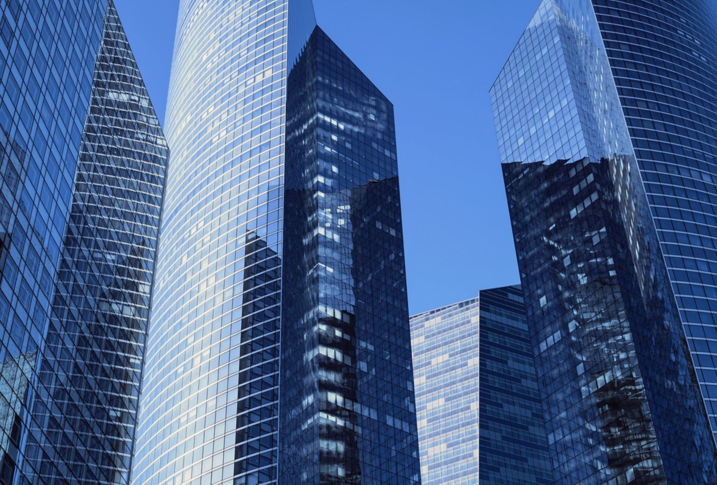 A low-angle architectural perspective of sleek glass office towers reflecting the blue sky.