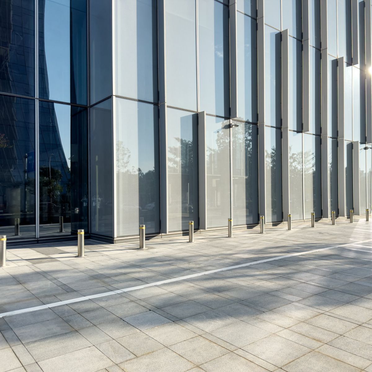 Low-angle perspective of a contemporary glass skyscraper exterior featuring reflective panels and a clean, paved pedestrian plaza.