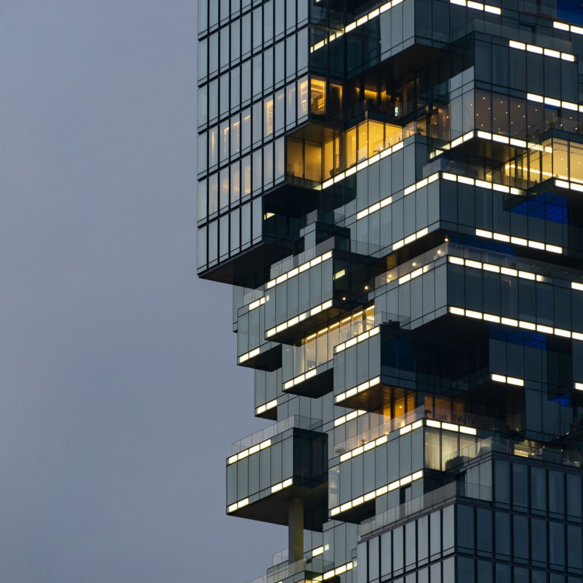 A low-angle view of a contemporary glass skyscraper featuring a unique, pixelated architectural design with illuminated windows against a twilight sky.