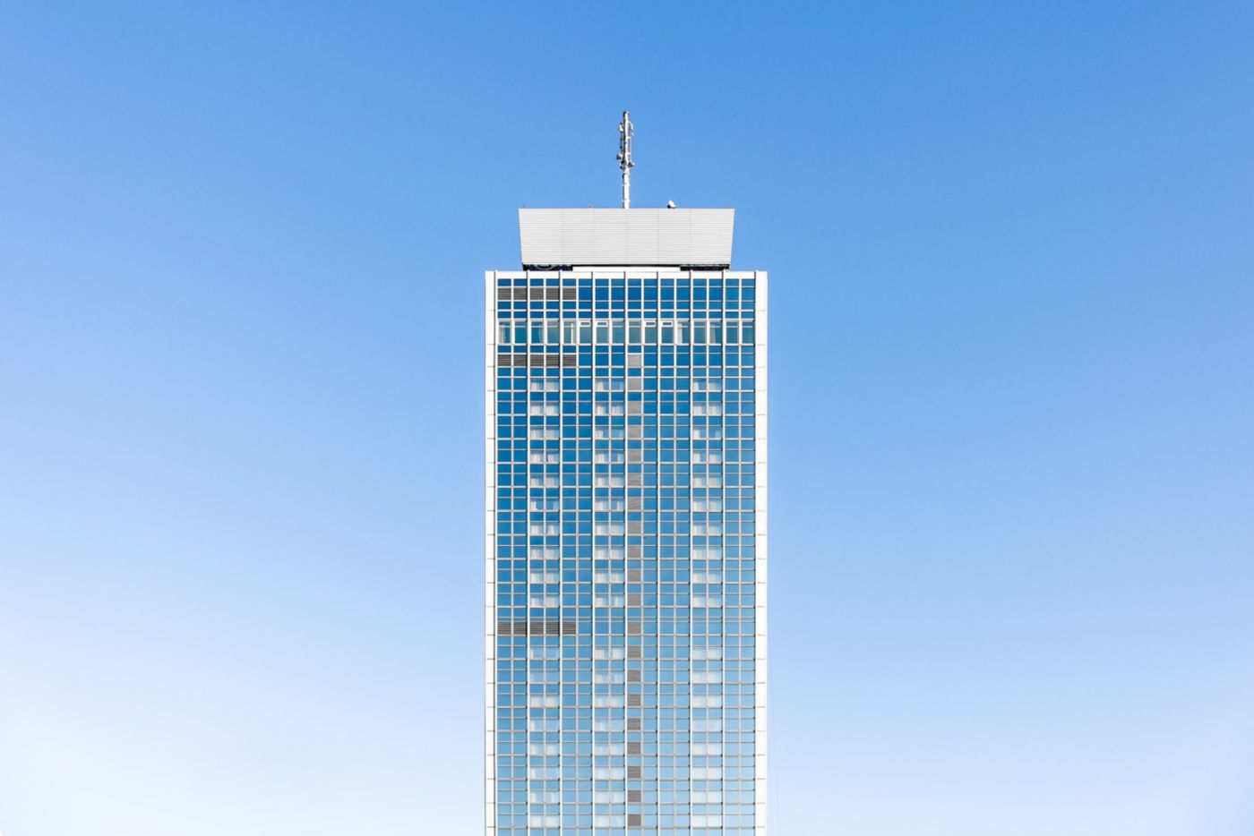 A symmetrical, low-angle shot of a glass skyscraper tower centered against a clear blue sky.