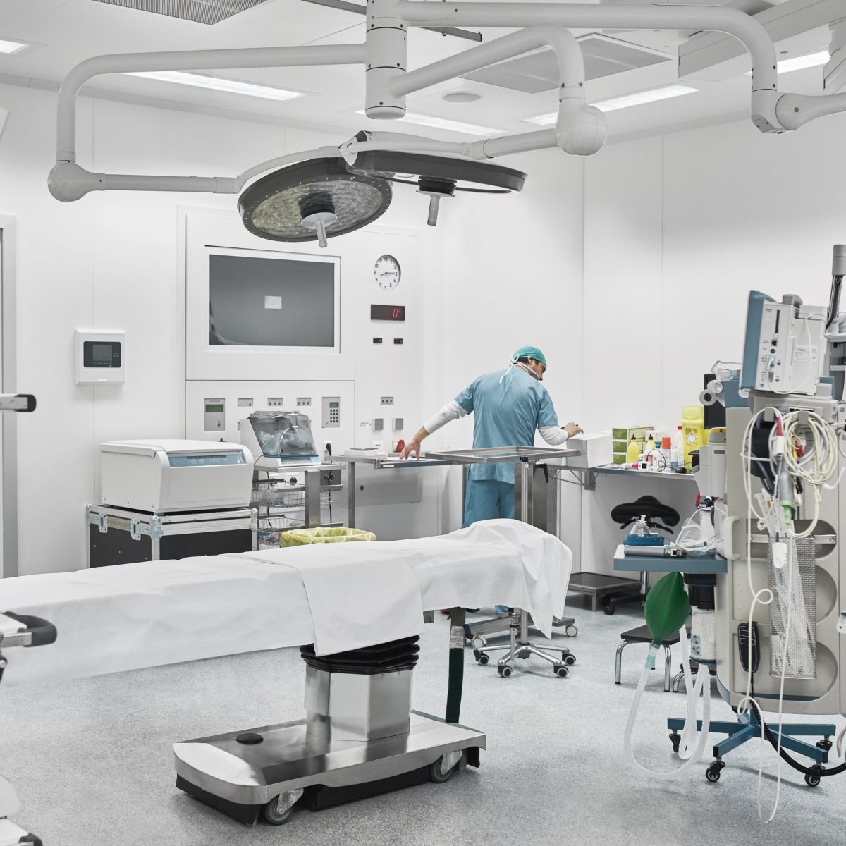 A healthcare professional prepares medical equipment in a contemporary, brightly lit operating room equipped with advanced surgical technology.