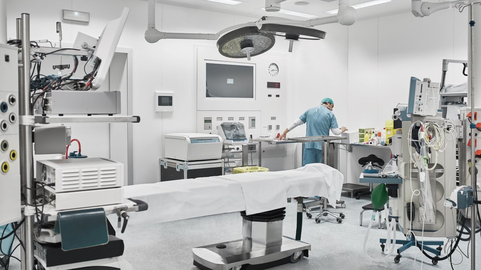 A healthcare professional prepares medical equipment in a contemporary, brightly lit operating room equipped with advanced surgical technology.