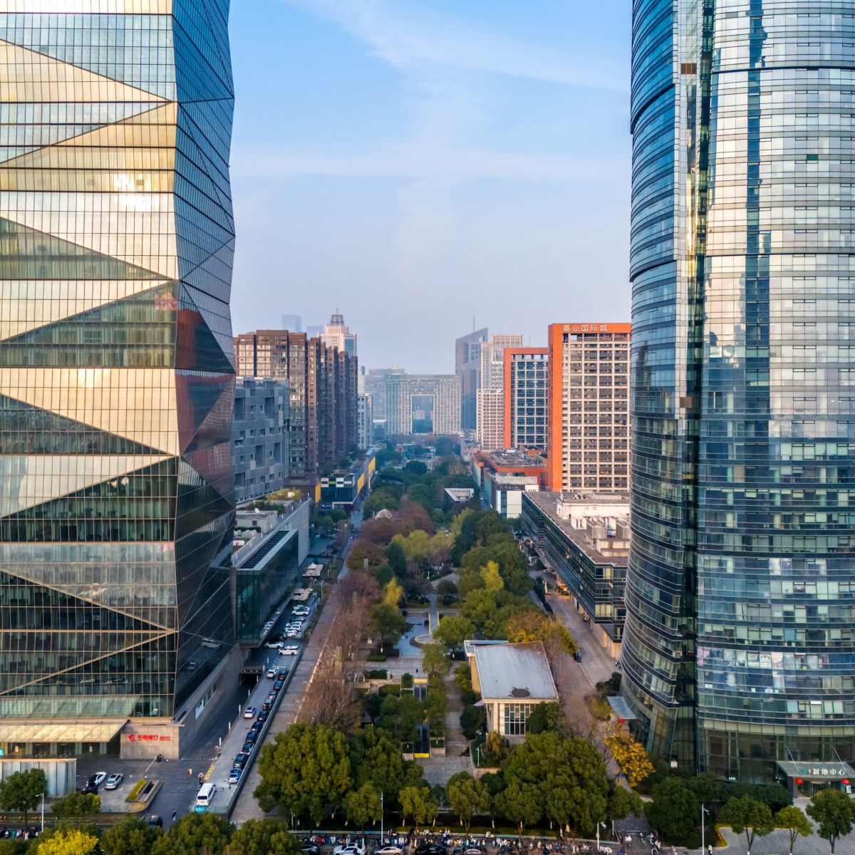 Elevated view of modern corporate glass skyscrapers framing a landscaped pedestrian walkway within a bustling city center.