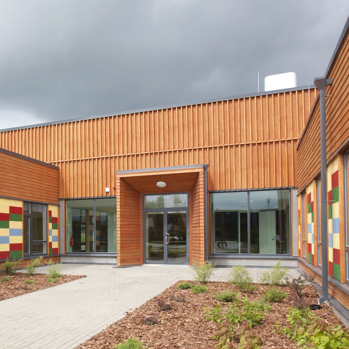 A low-angle shot of a modern architectural facility featuring vertical wood cladding and vibrant, multi-colored accents around large windows.