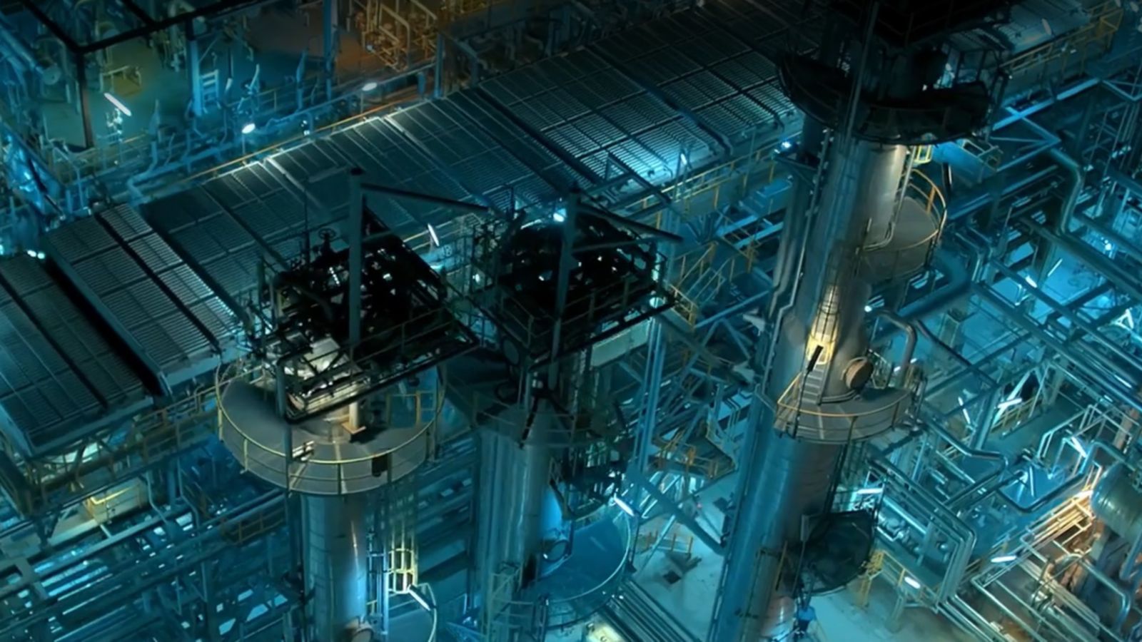 A stunning aerial shot of a modern industrial facility, featuring intricate machinery and vibrant neon blue lighting.