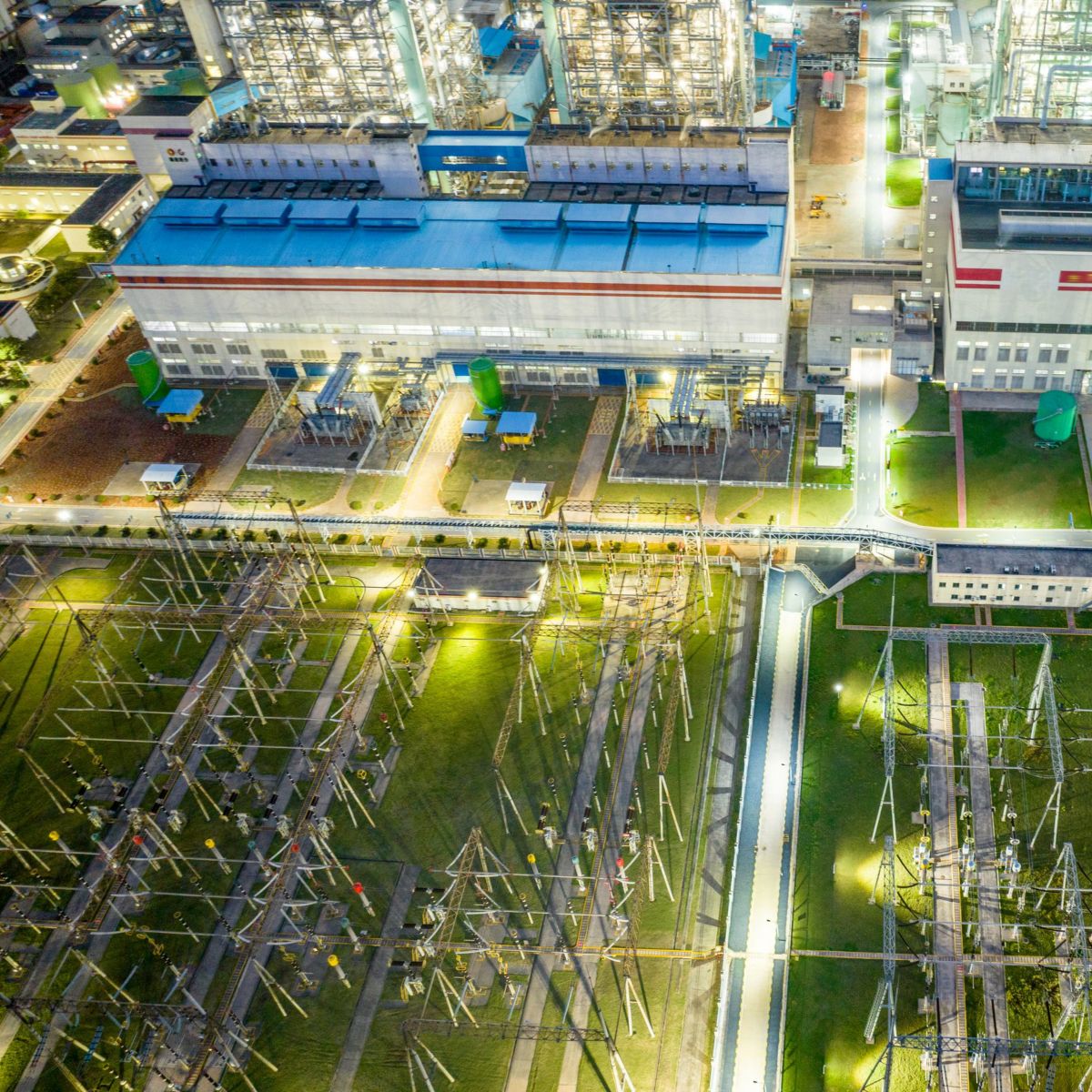 An aerial night view showcases a sprawling industrial power facility with illuminated infrastructure, vast electrical substations, and well-lit exterior grounds.