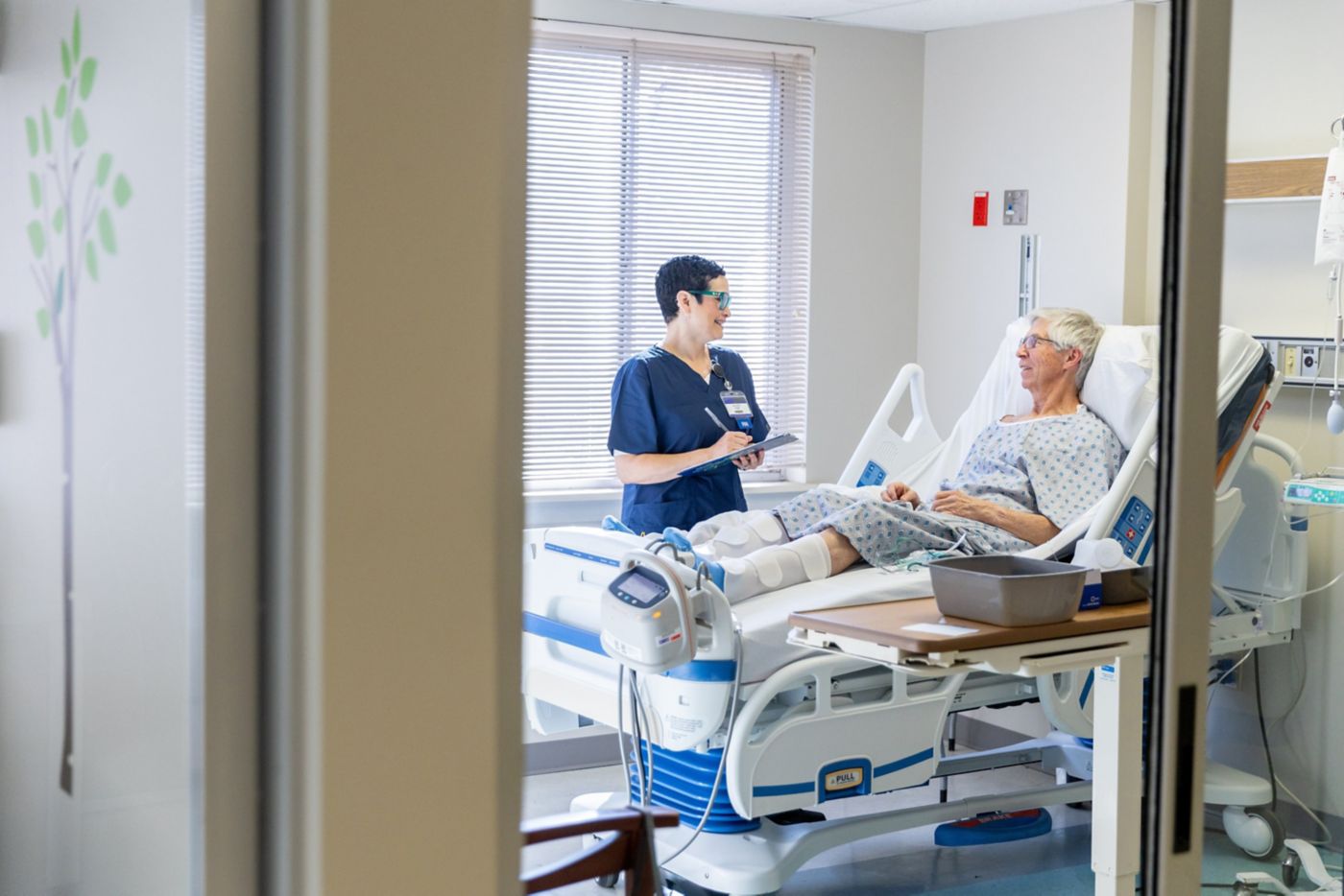 A friendly nurse in scrubs consults with an elderly patient resting in a hospital bed, focusing on compassionate healthcare communication.