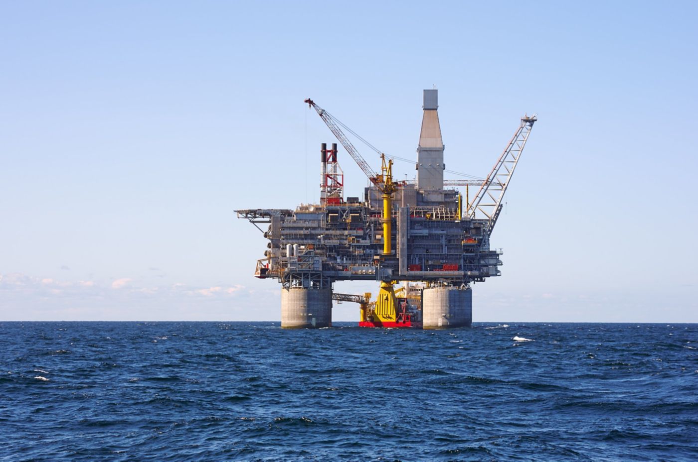 An industrial oil production platform stands in the middle of a vast, deep blue ocean under a clear sky.