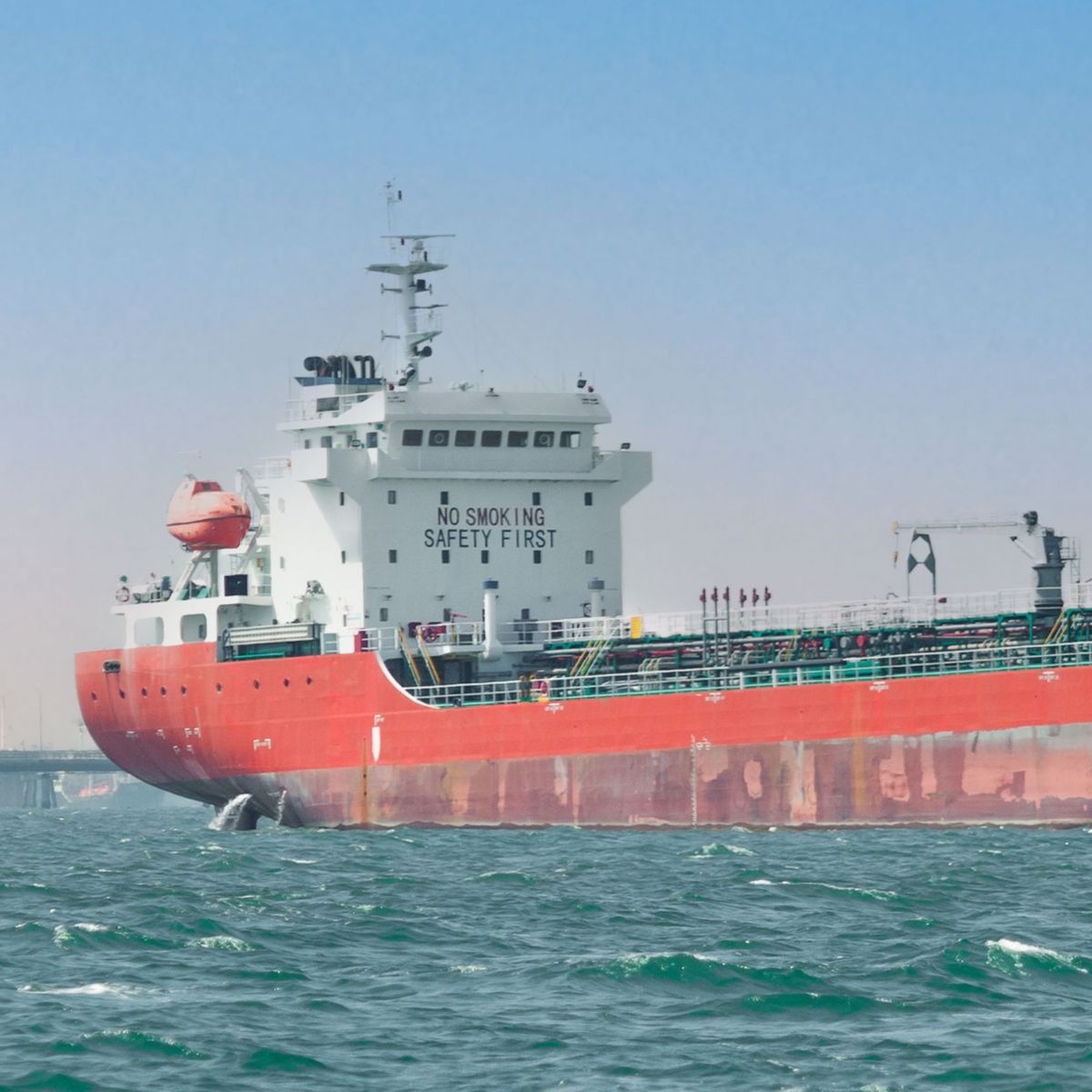 Marine tanker vessel traveling across open water near coastal infrastructure, supporting transportation and energy supply operations.