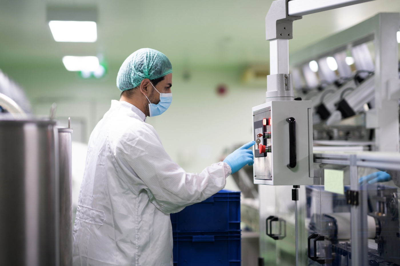 A technician in cleanroom attire operates industrial production equipment in a sterile pharmaceutical manufacturing facility.