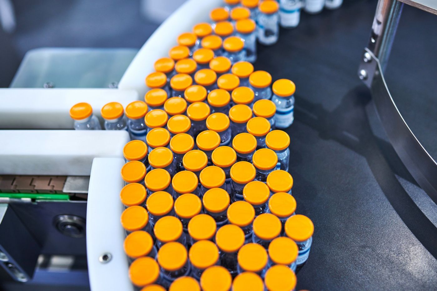 Pharmaceutical vials with orange caps moving along an automated conveyor belt system.