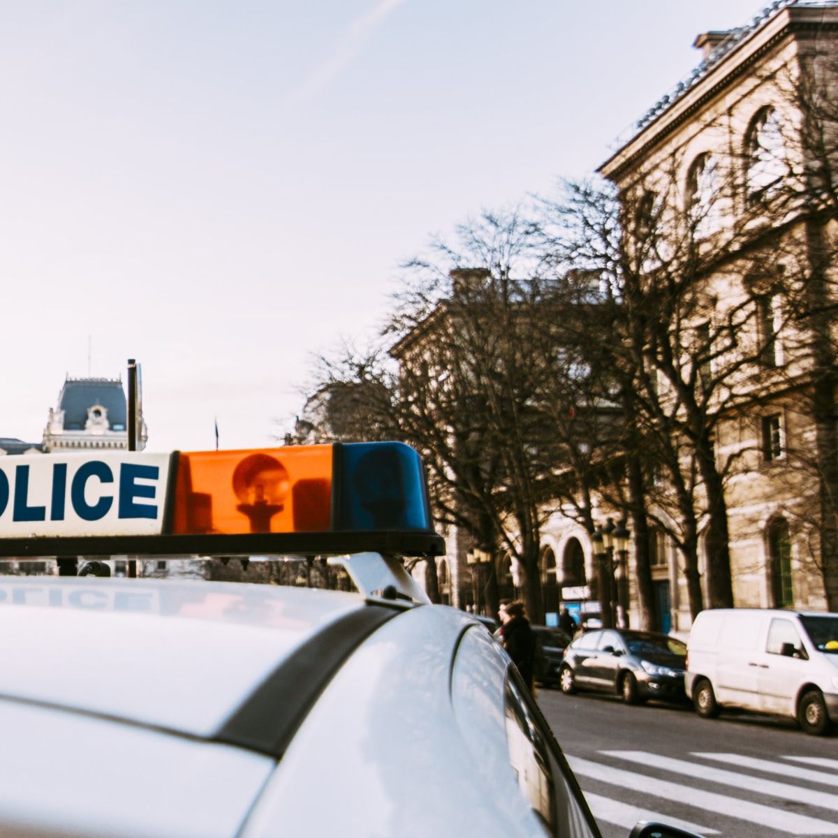 A low-angle rear view of a police car roof light bar parked on a city street during the day.
