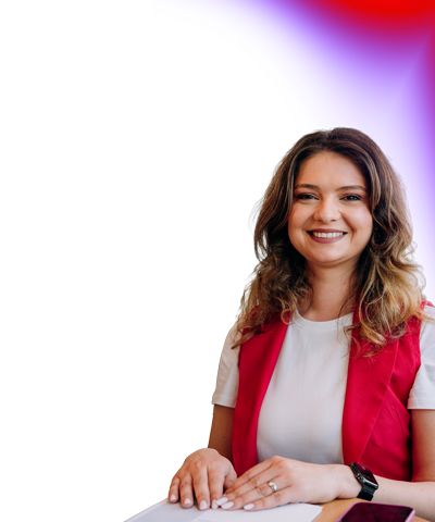 Professional portrait of an individual seated at a desk with a laptop against a clean background with subtle color gradient in corner.