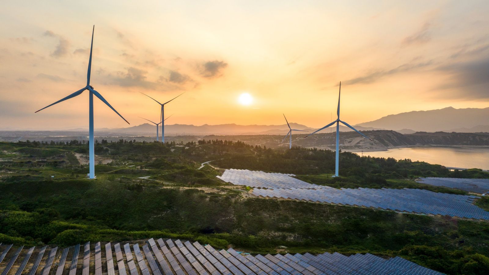 Aerial view of wind turbines and solar panels integrated into a scenic landscape at sunset.