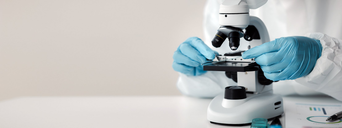 Blue-gloved hands adjust a sample beneath a laboratory microscope.