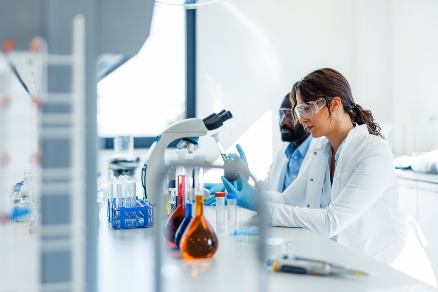 Diverse research team conducts diagnostic experiments using laboratory glassware and microscopy in a bright, modern corporate facility.