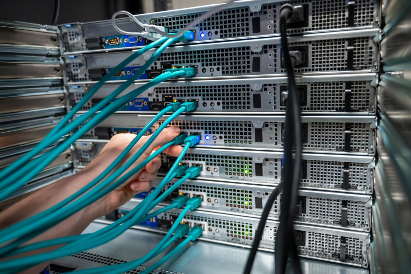 A technician connects a teal ethernet cable into a high-density server rack within a data center environment.