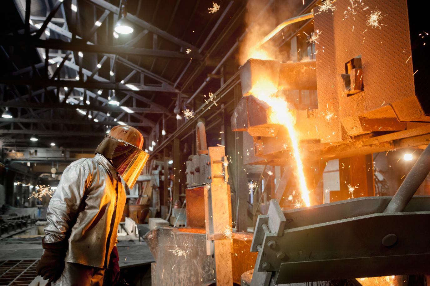 Worker operating furnace within heavy industrial environment.