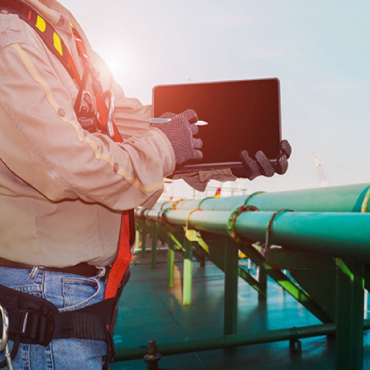 crew worker on oil tanker storage ship and hand holding ipad wearing safety full harness with green pipe line connect existing on deck.