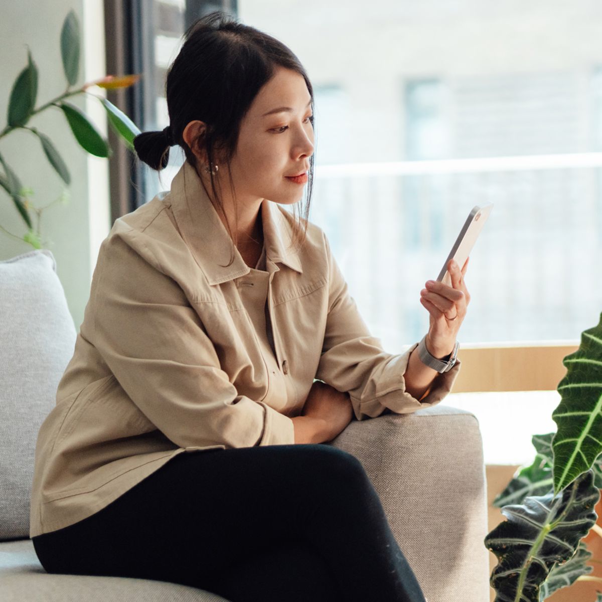 Person sitting near stacked boxes using a smartphone in a bright living 