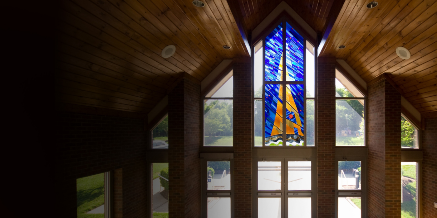 Sunlit interior featuring a vibrant stained glass window and vaulted wooden ceilin