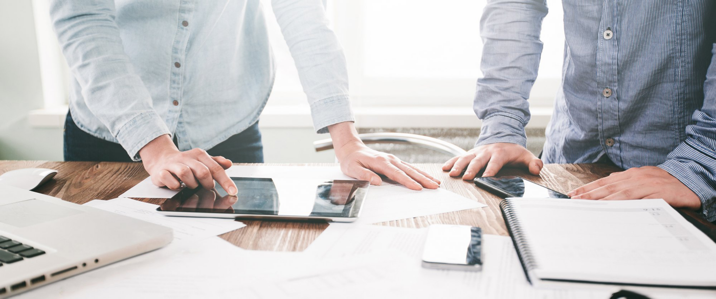 A group stands around a table using tablets, phones and printed materials during a planning session.