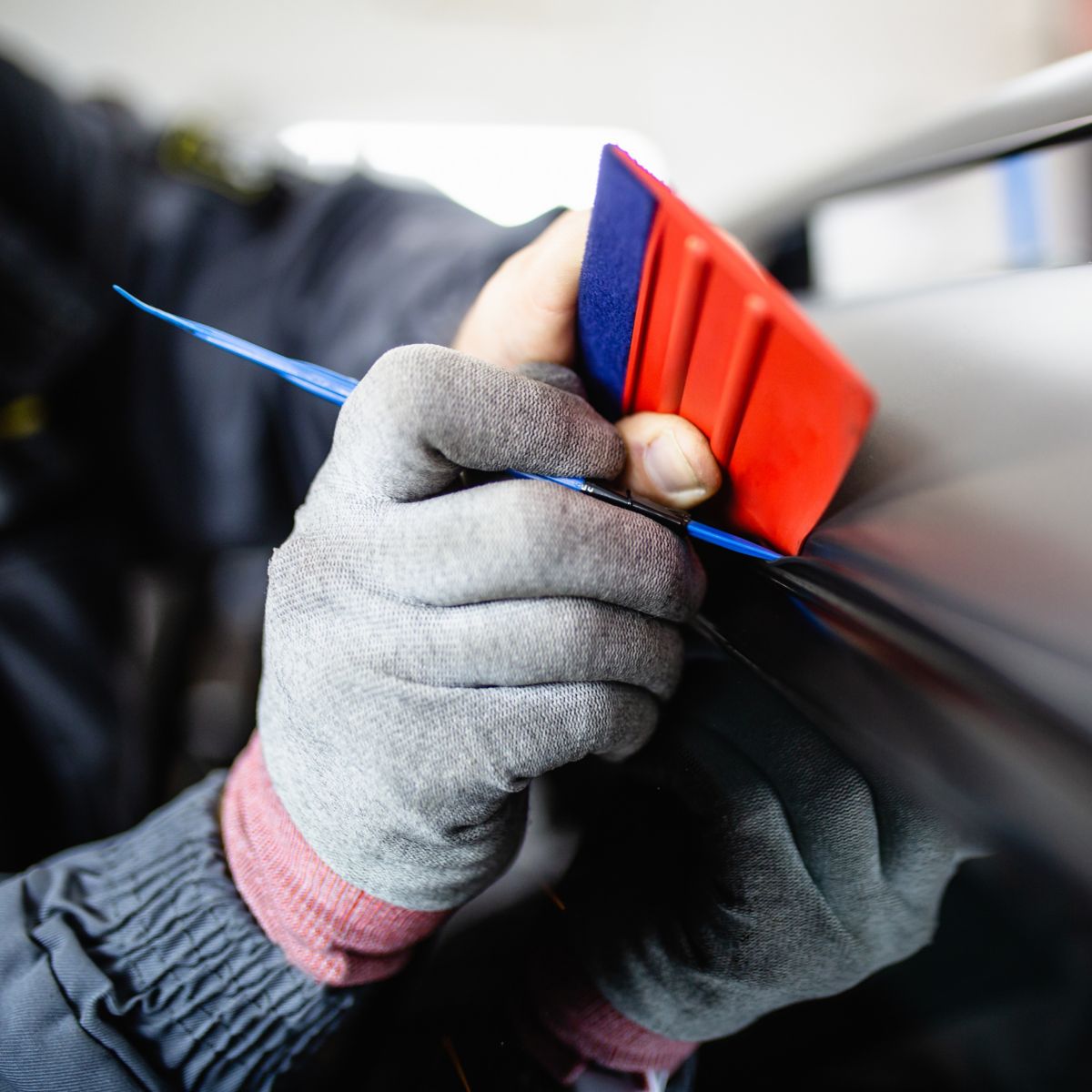 Car wrapping specialist putting vinyl foil or film on car. Selective focus.