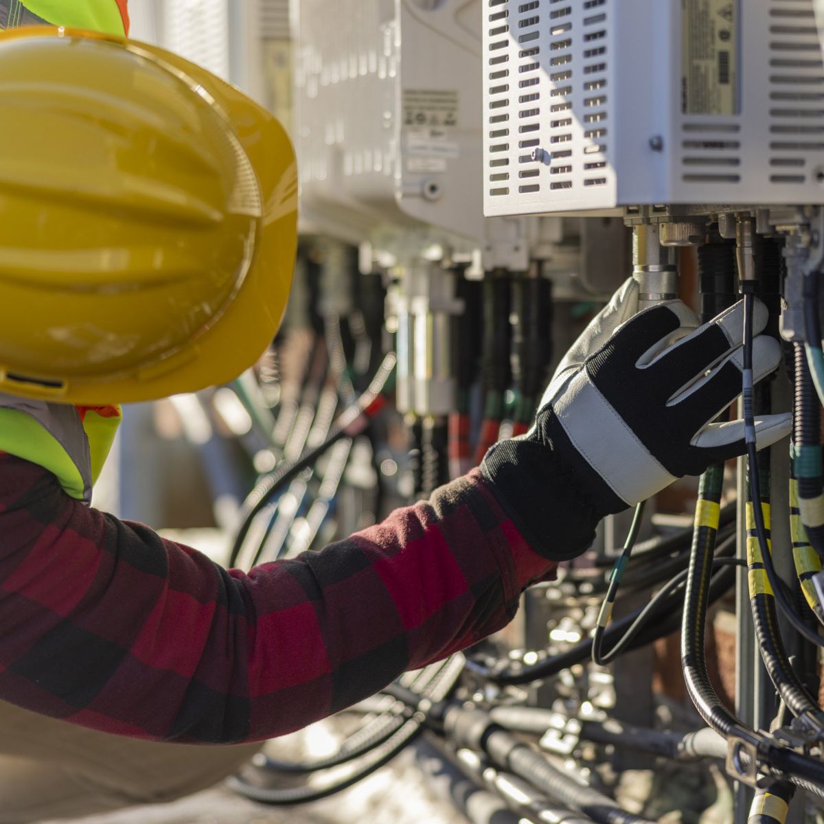 A field technician wearing safety gear connects wiring to industrial electrical equipment during a site installation.