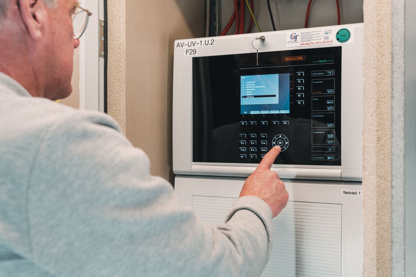 A technician interacts with the touchscreen interface of a fire alarm control unit in an industrial environment.