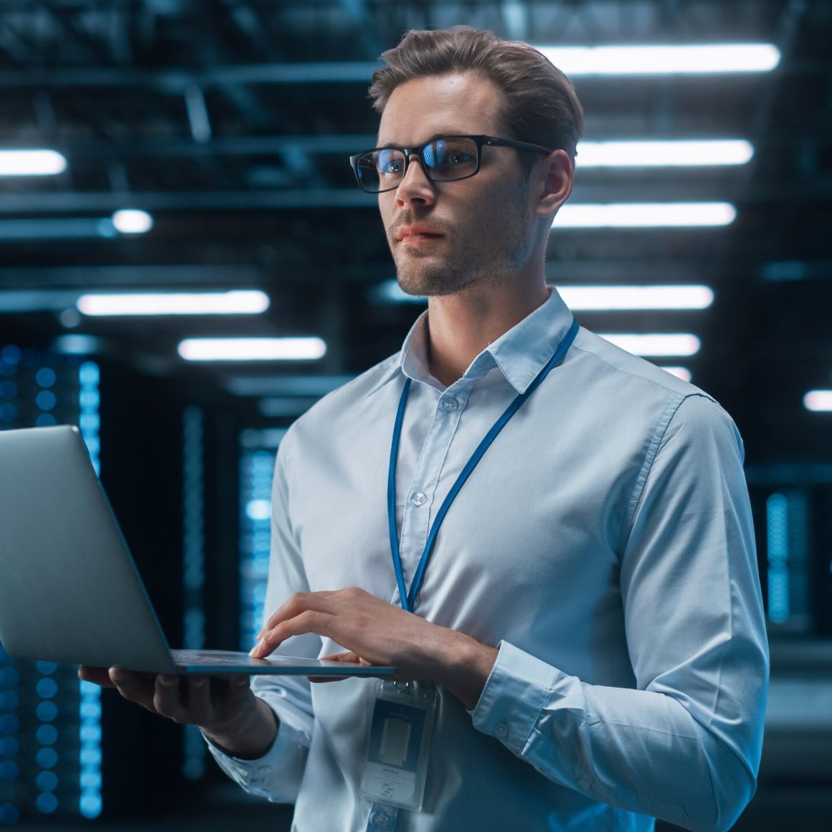 A professional holds a laptop in a data center, surrounded by illuminated server racks.