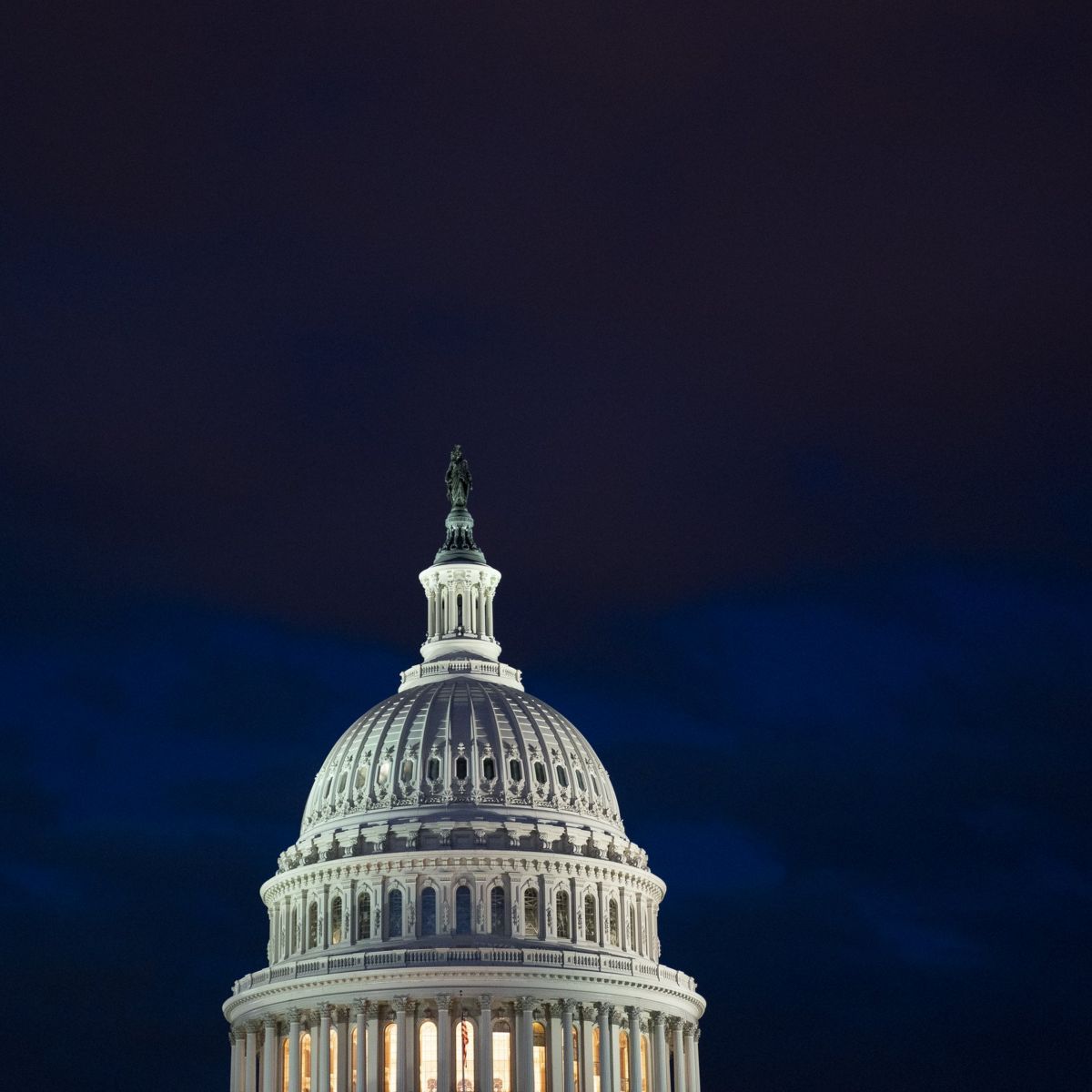 The illuminated United States Capitol dome stands against a dark, dramatic evening sky.