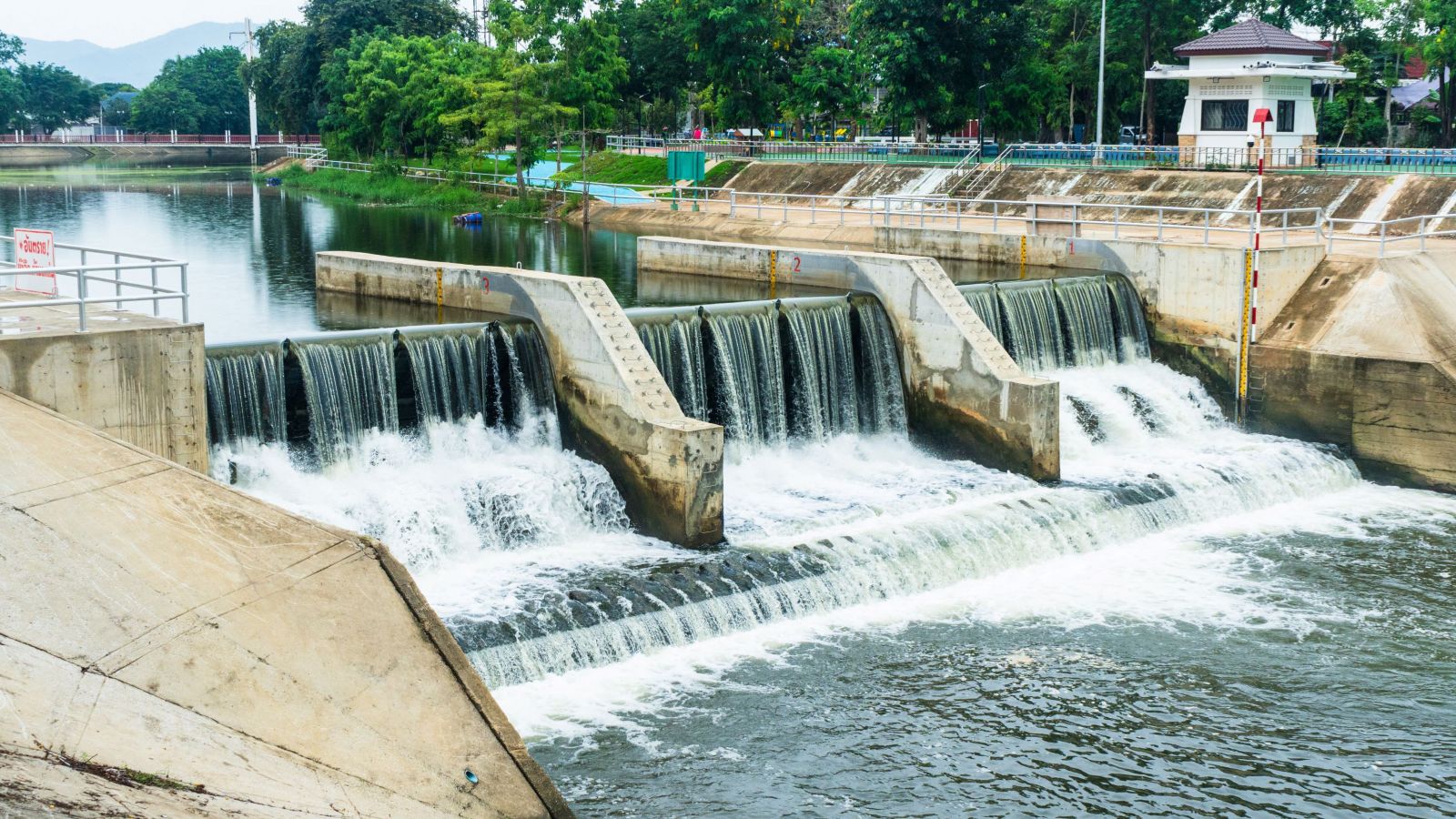Water flows over a control structure, creating small waterfalls in a serene environment surrounded by greenery.