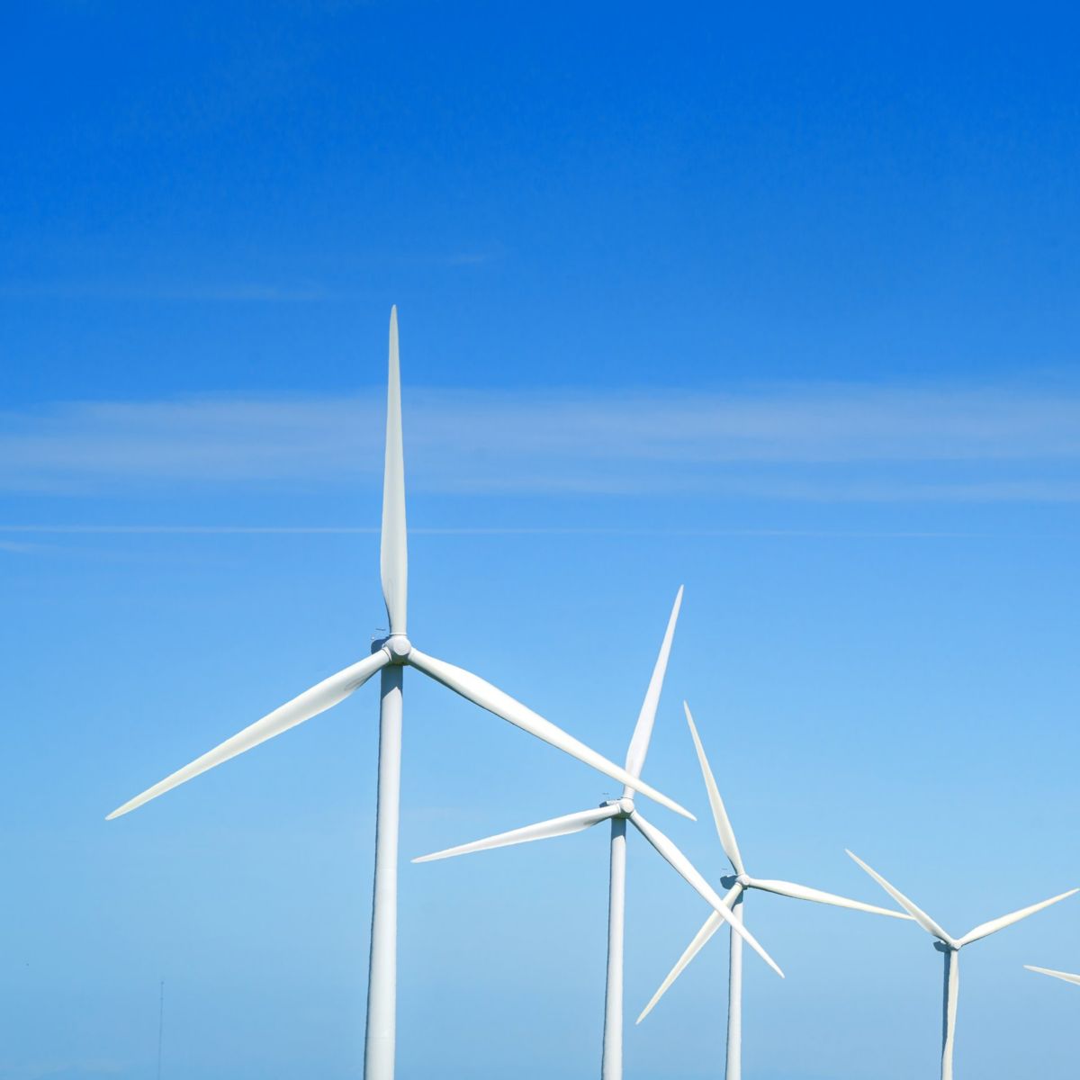 A row of wind turbines stands against a vibrant blue sky in a scenic, rolling green landscape.