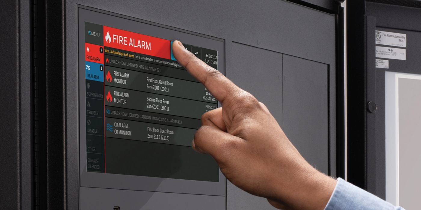 A close-up of a hand pressing a control button on an ONYX Fire Alarm panel. 