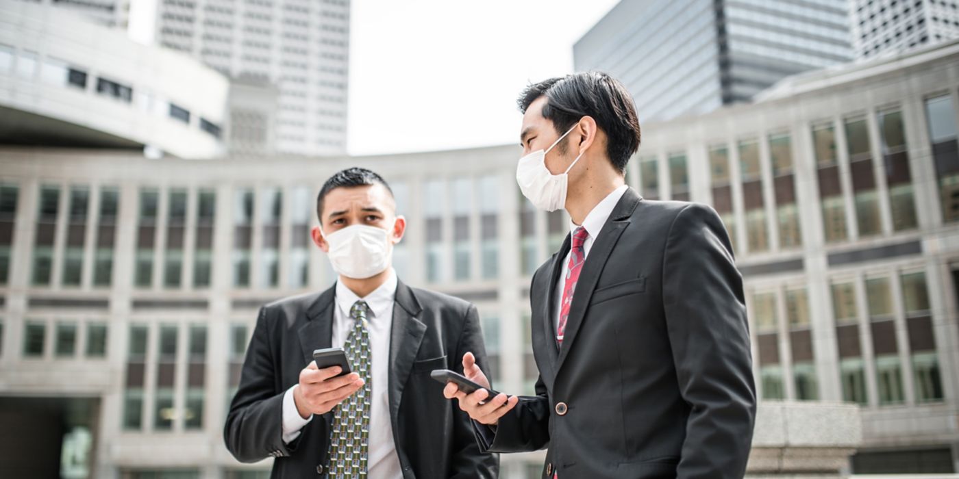 Two men outdoors with masks on, checking their smartphones.